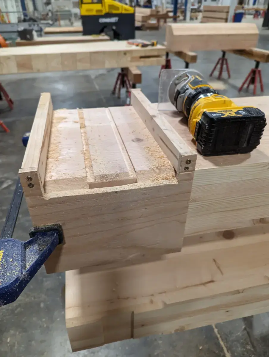Wooden router jig fitted over the end of a timber beam with a cordless router resting on top